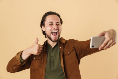 Bej arka planda izole edilmiş cep telefonuyla selfie çeken mutlu bir adamın görüntüsü