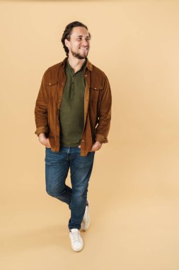 Bej arka planda izole edilmiş, gülümseyen ve yan bakan kotlu neşeli genç adam görüntüsü