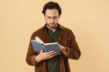 Gözlüklü ciddi, tıraşsız bir adamın bej arka planda izole edilmiş kitap okuması.