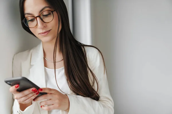 Foto Empresária Satisfeita Óculos Usando Telefone Celular Enquanto Inclina Parede — Fotografia de Stock