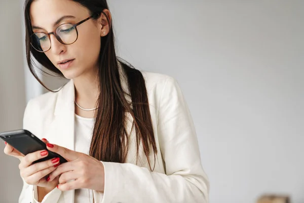 Photo Concentrated Businesswoman Eyeglasses Using Mobile Phone While Standing Indoors — Stock Photo, Image