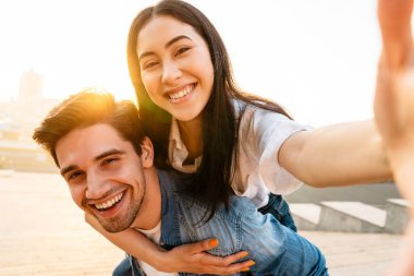 Neşeli, çok kültürlü çiftlerin gezintiye çıkmaları ve dışarıda yürürken selfie çekmeleri.