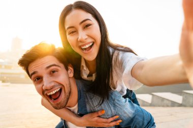 Neşeli, çok kültürlü çiftlerin gezintiye çıkmaları ve dışarıda yürürken selfie çekmeleri.