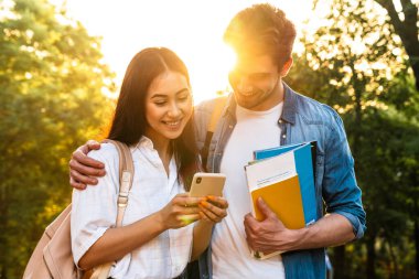 Green Park 'ta yürürken cep telefonu kullanan ve gülümseyen neşeli, çok kültürlü bir çift.