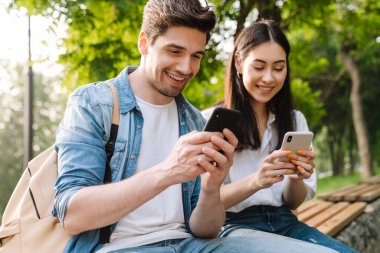 Cep telefonu kullanan ve parkta bankta otururken gülümseyen çok kültürlü bir çift görüntüsü