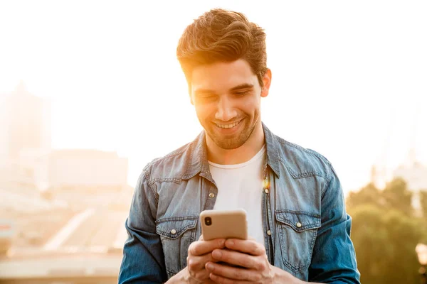 Photo Joyful Handsome Man Smiling Using Mobile Phone While Walking — Stock Photo, Image