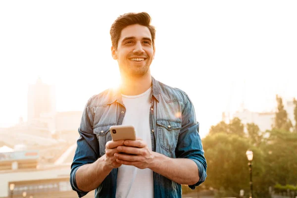 Foto Hombre Guapo Alegre Sonriendo Usando Teléfono Móvil Mientras Camina —  Fotos de Stock