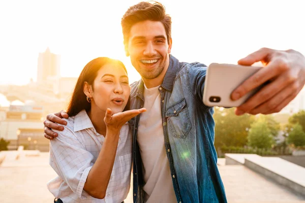 Wizerunek Szczęśliwej Wielokulturowej Pary Dmuchającej Pocałunek Powietrza Robiącej Selfie Komórce — Zdjęcie stockowe