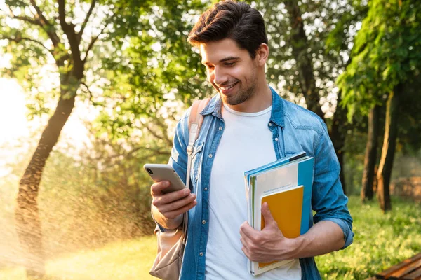 Foto Sorridente Uomo Studente Non Rasato Con Quaderni Utilizzando Smartphone — Foto Stock