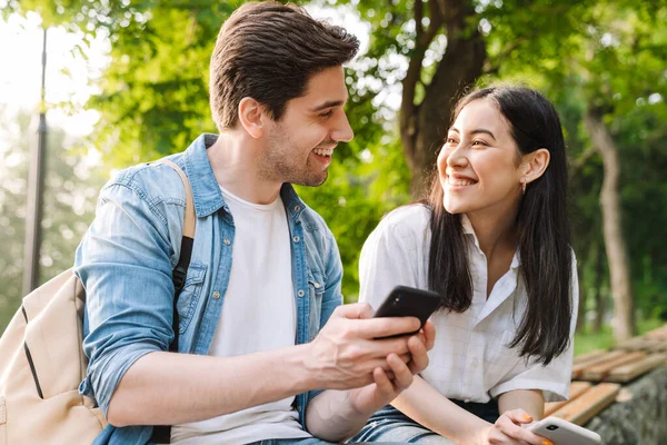 Obrázek Potěšené Multikulturní Pár Pomocí Mobilních Telefonů Úsměvem Při Sezení — Stock fotografie