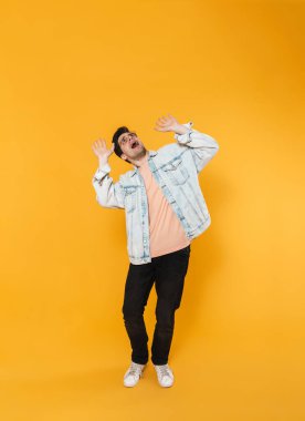 Yukarı bakan korkmuş genç adamın fotoğrafı. Sarı arka planda izole edilmiş elleri kusuyor.