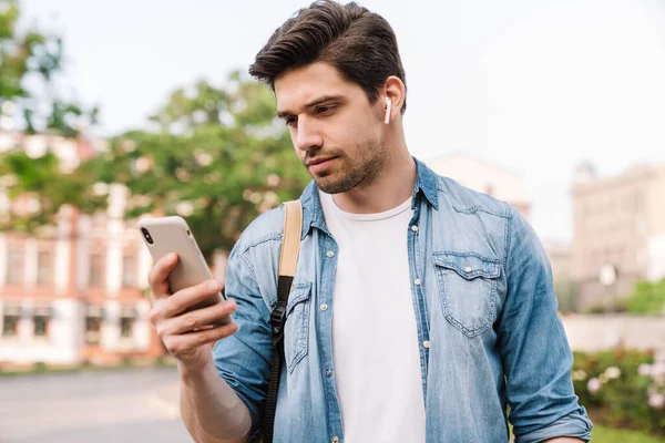 Foto Uomo Concentrato Con Auricolare Wireless Utilizzando Cellulare Mentre Cammina — Foto Stock