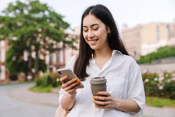Zdjęcie Szczęśliwej Azjatyckiej Kobiety Korzystającej Telefonu Komórkowego Pijącej Kawę Wynos — Zdjęcie stockowe
