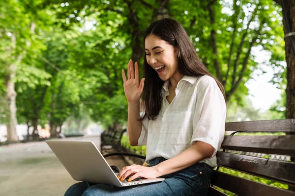 Photo Laughing Asian Woman Using Laptop Waving Hand While Sitting — Stock Photo, Image