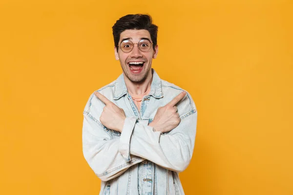 Photo Delighted Young Man Eyeglasses Pointing Fingers Aside Isolated Yellow — Stock Photo, Image