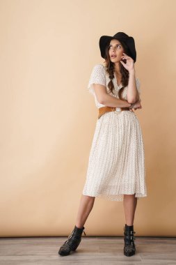 Esmer, güzel bir kadının bej arka planda poz verirken ve yukarı bakarken tam boy fotoğrafı.