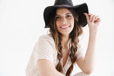 Beyaz arka planda izole edilmiş kameraya bakarken gülümseyen şapkalı neşeli, baştan çıkarıcı kadının fotoğrafı.