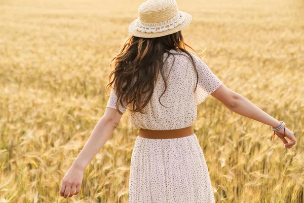 夏の日に麦畑で踊るわら帽子のかわいいブルネットの女性の後ろからの写真 — ストック写真