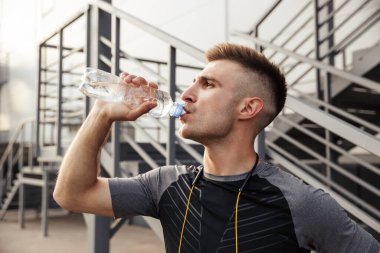 Açık şehir merdivenlerinin yanında spor yaparken tıraş edilmemiş beyaz bir sporcunun su içişi.