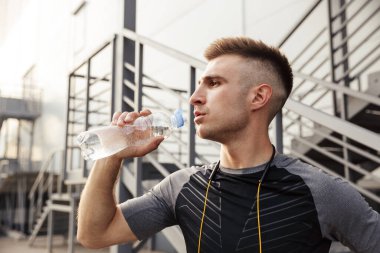 Açık şehir merdivenlerinin yanında spor yaparken tıraş edilmemiş beyaz bir sporcunun su içişi.