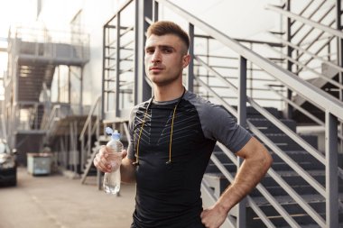 Açık şehir merdivenlerinin yanında spor yaparken tıraş edilmemiş beyaz bir sporcunun su içişi.
