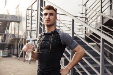 Açık şehir merdivenlerinin yanında spor yaparken tıraş edilmemiş beyaz bir sporcunun su içişi.
