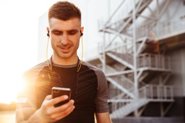 Şehir dışında çalışırken cep telefonu ve kulaklık kullanan genç sporcunun görüntüsü