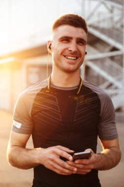 Açık hava alanında çalışırken cep telefonu ve kulaklık kullanan gülen sporcu görüntüsü