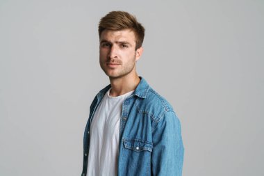 Gri arka planda izole edilmiş kameraya bakan ve poz veren vahşi traşsız bir adamın portresi.