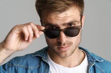 Güneş gözlüklü yakışıklı bir adamın portresi. Gri arka planda izole edilmiş kameraya bakıyor ve poz veriyor.