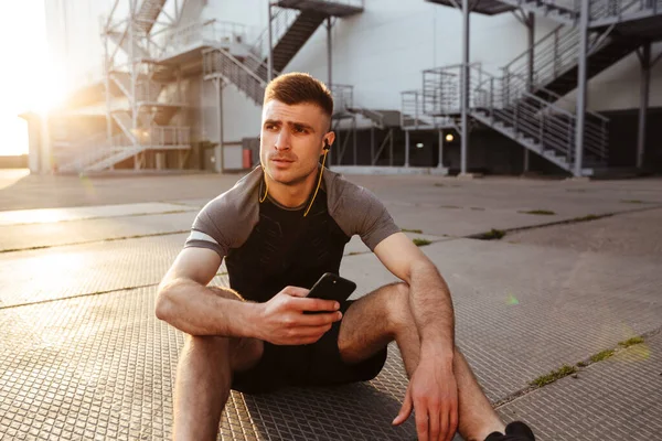 Imagem Jovem Esportista Caucasiano Usando Celular Fones Ouvido Enquanto Sentado — Fotografia de Stock