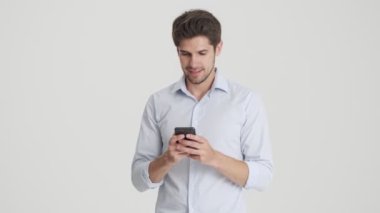 Mutlu bir adam, mutlu olurken akıllı telefonunu kullanır ve beyaz arka planda tek başına duran, kazanan bir jest yapar.