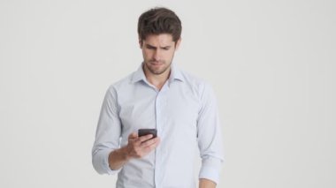 Yakışıklı bir adam, beyaz arka planda izole bir şekilde durup, sevinçle akıllı telefondan konuşurken ve kazanan hareketi yaparken iyi haberler alıyor.