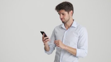 Çekici bir adam, beyaz arka planda izole bir şekilde duran akıllı telefonuyla sevdiği bir şeyi yazıyor.