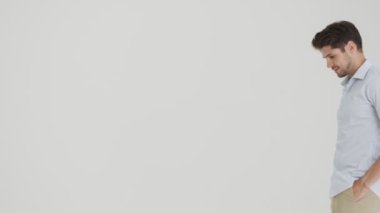 Pozitif bir genç adam bir taraftan diğer tarafa yürüyor ve beyaz arka planda izole edilmiş kameraya barış hareketi gösteriyor.