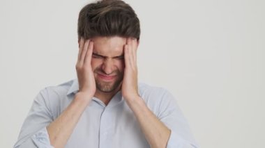 Hoşnutsuz bir gencin yakın plan görüntüsü, beyaz arka planda izole edilmiş bir baş ağrısı hissederken şakaklarına masaj yapıyor.