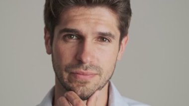 Beyaz arka planda yalnız duran yakışıklı bir gencin yakın çekim görüntüsü kameraya yansıyor.