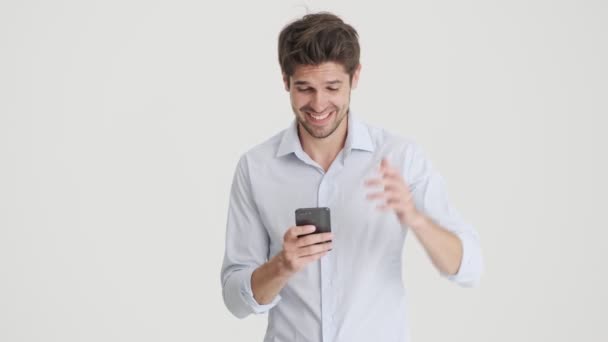 Улыбающийся Человек Использует Свой Смартфон Стоящий Изолированно Белом Фоне — стоковое видео