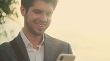 Mutlu yakışıklı işadamı gün batımında akıllı telefon kullanıyor.