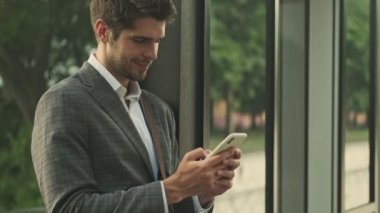 Gülümseyen yakışıklı işadamının binanın yanında dururken akıllı telefon kullanışının yan görüntüsü