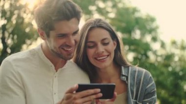 Parkta yan yana dururken akıllı telefon kullanan mutlu genç çift.