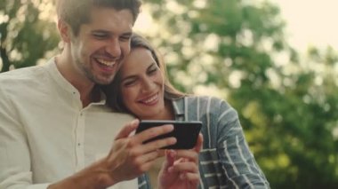Parkta yan yana dururken akıllı telefon kullanan neşeli genç çift.