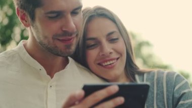 Parkta yan yana dururken akıllı telefon kullanan tatmin olmuş genç çift.