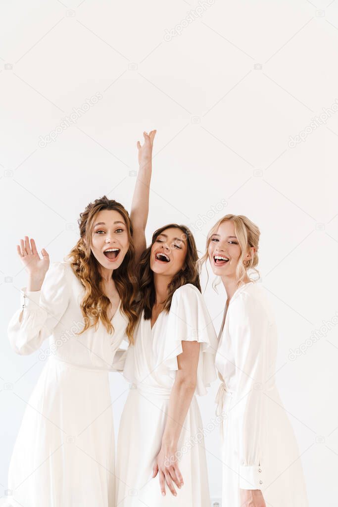 Photo of joyful charming three women dancing and laughing at camera isolated over white wall