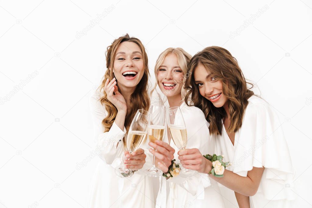 Photo of joyful beautiful bridesmaids laughing and drinking champagne isolated over white wall