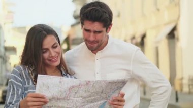 Gülümseyen genç çift caddede yan yana dururken şehir haritasını inceliyor.