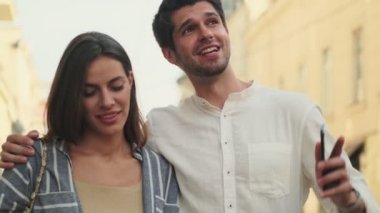Akıllı telefon kullanan ve sokakta yürürken etrafa bakınan mutlu genç çift.