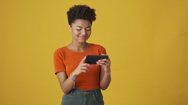 微笑迷人的非洲女人玩智能手机 对黄色的背景感到惊讶 — 图库视频影像