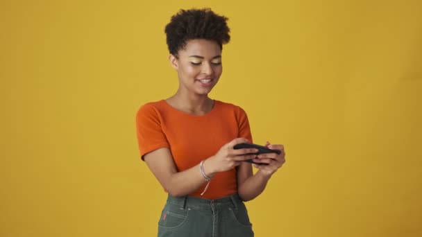 Radosna Atrakcyjna Afrykańska Kobieta Grająca Smartfonie Bawiąca Się Żółtym Tle — Wideo stockowe