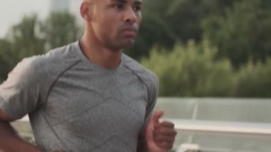 Odaklanmış genç bir Afrikalı adamın yakın çekim görüntüsü sabah köprüde koşuyor.